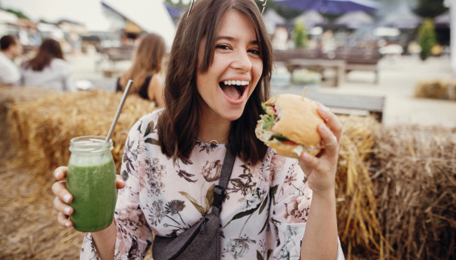 Happy woman holding burger and drink in summer street