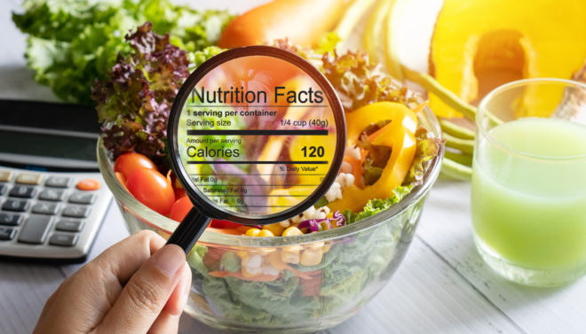 nutritional information concept. hand use the magnifying glass to zoom in to see the details of the nutrition facts from a salad bowl