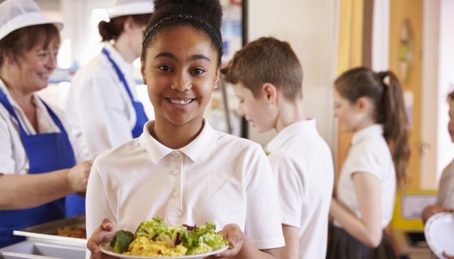 Black schoolgirl holds a plate of food in a school cafeteria